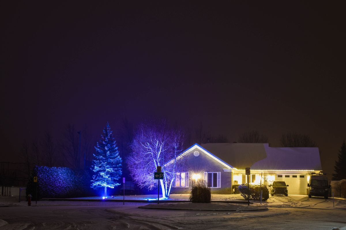 A house exterior with snowy roofline and permanent holiday lights illuminated at night